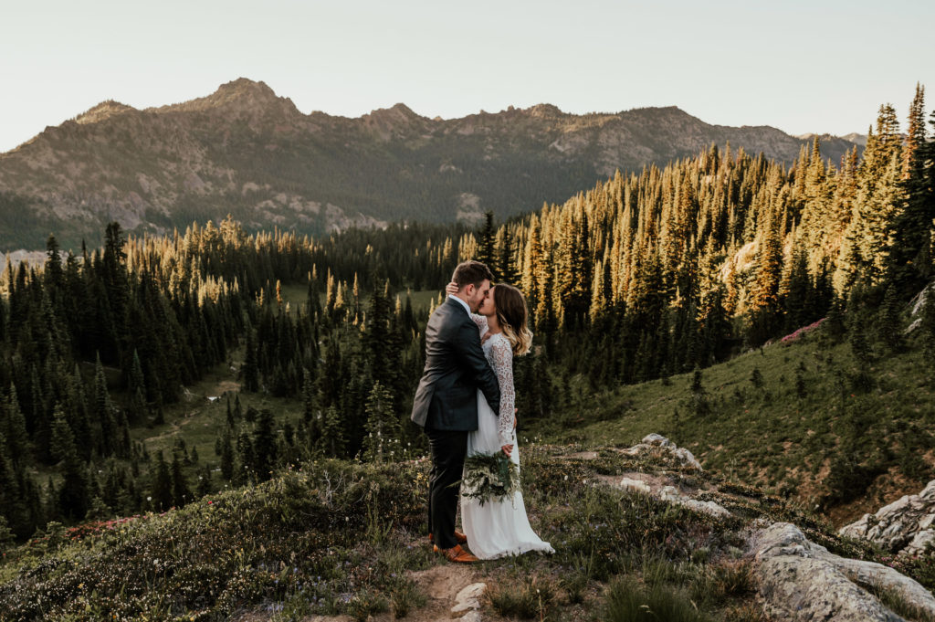 A couple in wedding attire kisses on a trail in Mount Rainier National Park for their adventurous elopement.