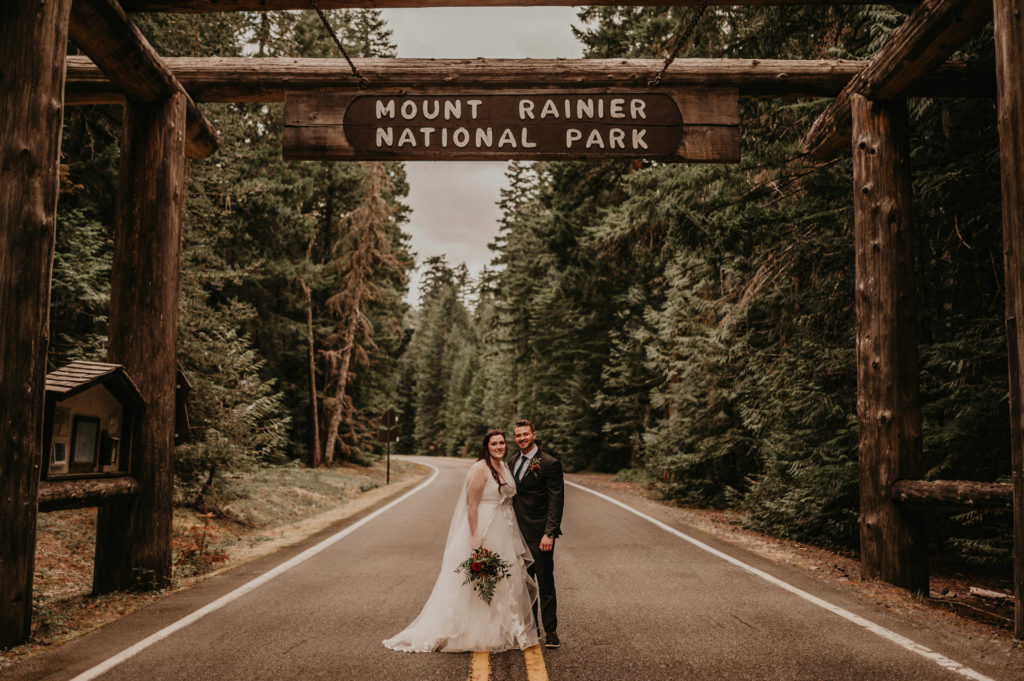 A couple stands underneath the Mount Rainier National Park entrance sign during their elopement.