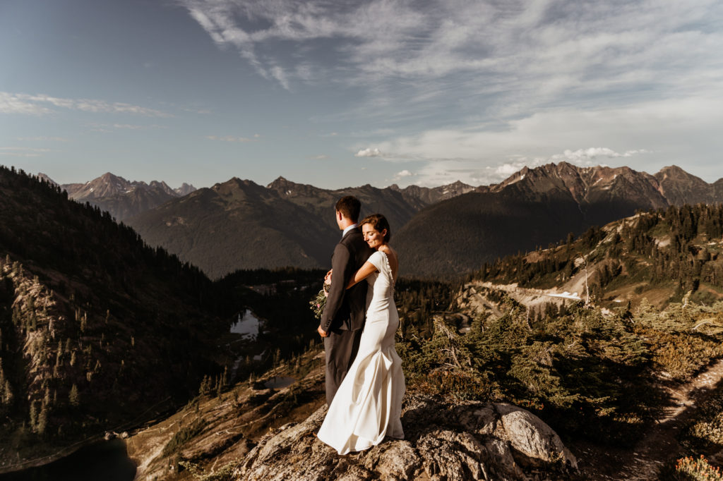 A woman in a white wedding dress hugs her husband, wearing a suit, in North Cascades National Park, for their elopement.
