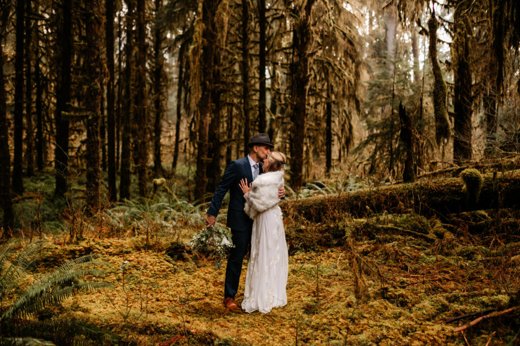 A bride and groom in wedding attire hugging each other in the rainforest for their Olympic National Park elopement.