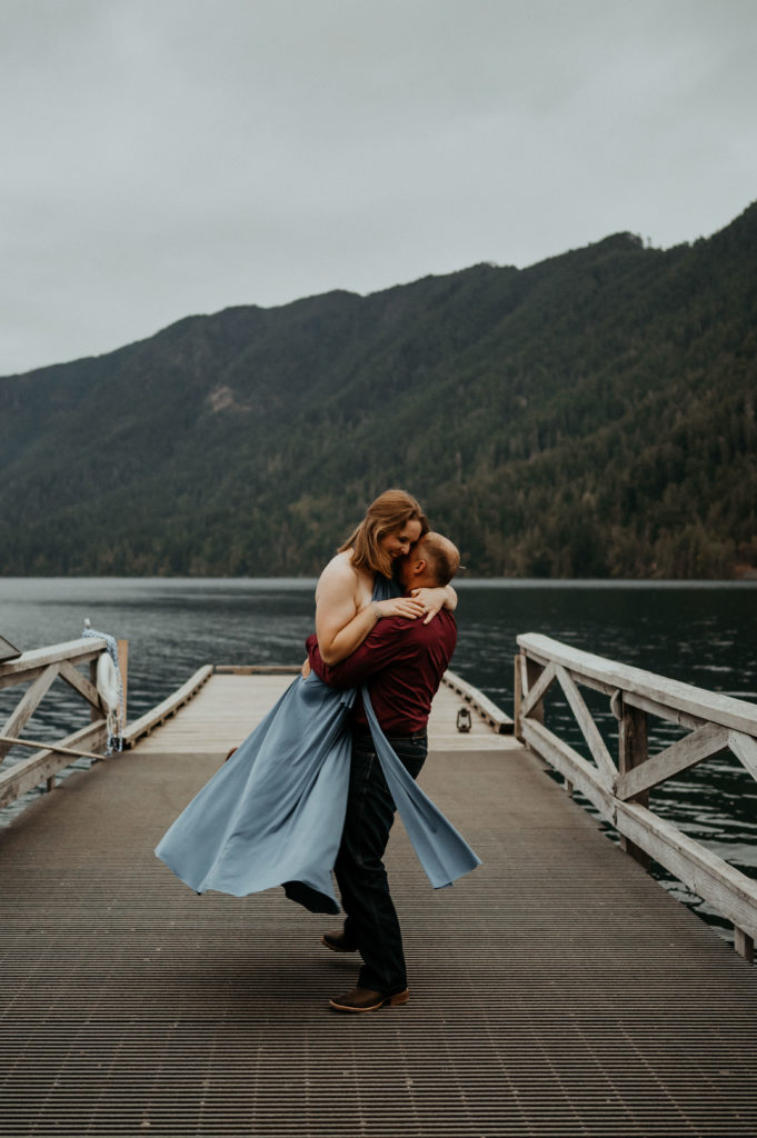 A man and woman dancing on a lake side dock in Olympic National Park for their engagement photography session.