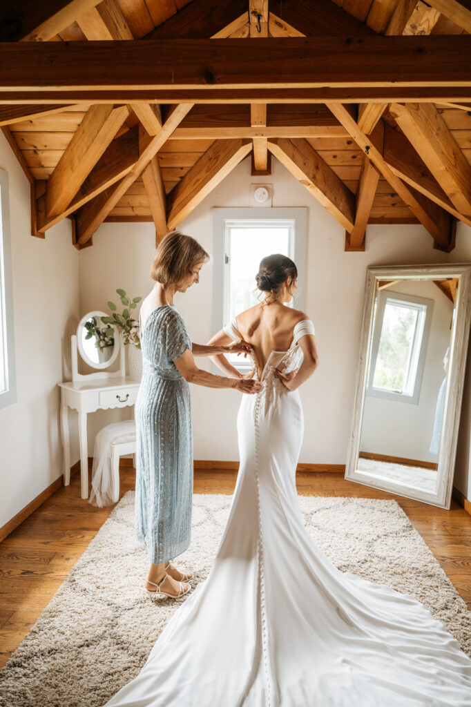 A bride receives help putting on her dress from her mother on her wedding day at Chateau Lill.